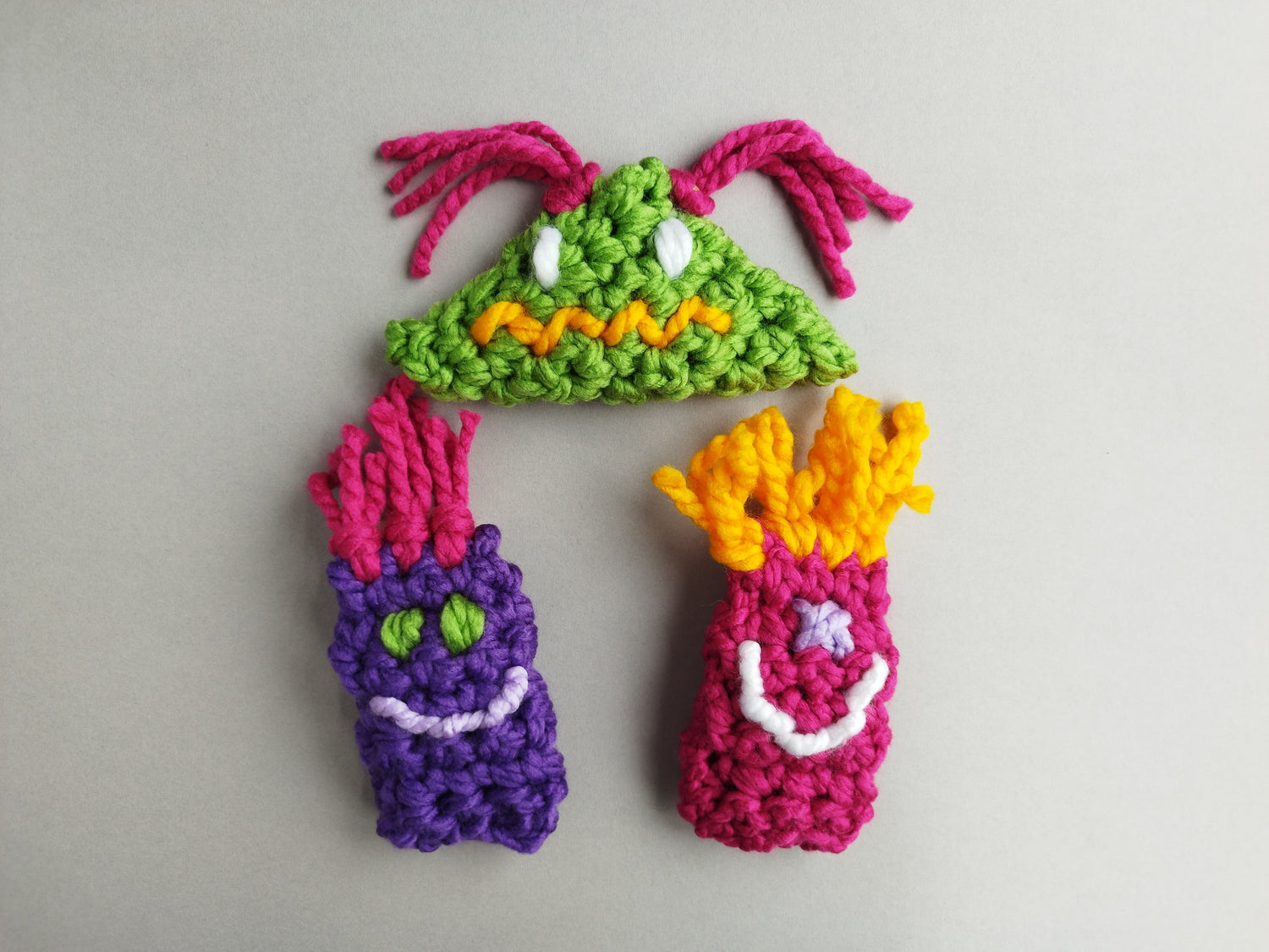 Three colorful crochet creatures arranged on a plain light gray background.
